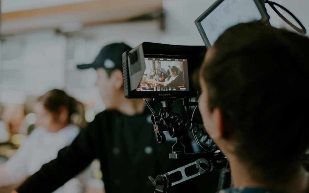 A camera operator filming on set, the monitor showing the shot